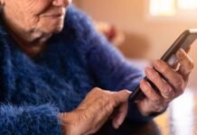 Access The Latest Technology With AT&T Phones Specifically Designed For Seniors. Elderly woman using mobile phone while sitting at living room home. Grandmother