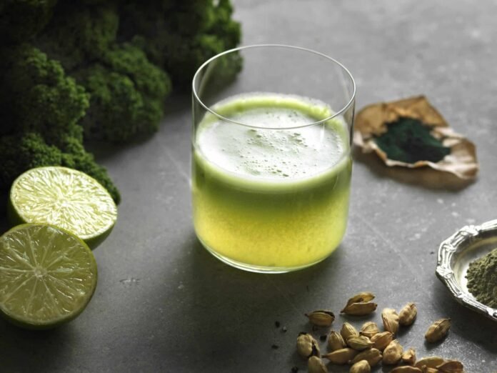 High angle view of green raw juice with halved lime and nutritional supplement